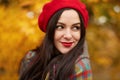 Fabulous romantic woman with long dark hair wearing red beret on blurred autumn background. Girl in forest with orange autumn