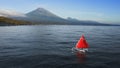 Fabulous scarlet red sail white Jukung boat floating on quiet ocean water near sea shore with huge volcano in summer