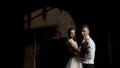 Fabulous wedding couple standing against black wall with the shadow from the metal gate. Action. Portrait of young bride