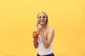 Fabulous woman in sunglasses wearing white t-shirt while holding glass of juice isolated over yellow background Royalty Free Stock Photo