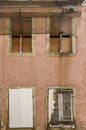 Facade of abandoned, dilapidated house with 4 boarded windows, shutters, boards and flow as protection from falling tiles and