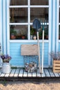 Facade blue home with garden tools: shovel, pitchfork, rake, firewood and pots flowers. Cozy Autumn decor veranda house. Gardening Royalty Free Stock Photo