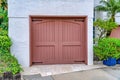 Facade of garage with brown wooden hinged door against white wall and foliage