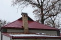 Part of the house with a red tile roof in the snow and a brick wall against the background of wood and sky Royalty Free Stock Photo