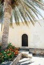 Facade of a house with a small wooden door in a tropical village. Entrance to the building, with a palm tree and flowering plants Royalty Free Stock Photo