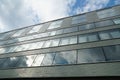 A facade of a modern corporate building with large glass surface in upward perspective with sky and clouds reflected on the facad