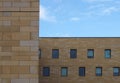 Facade of a modern stone building with geometric repeating pattern of small windows and blue sky