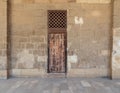 Old abandoned stone bricks wall with one weathered wooden door and wooden grid window, Old Cairo, Egypt