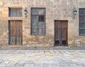 Facade of old abandoned stone bricks wall with wooden doors , windows covered with iron bars and lanterns