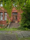 Facade of old brick building with concrete stairs, barred doors and windows and full of bushes