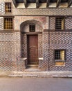 Black and red bricks wall with white seam and wooden arched entrance gate with inner small door Royalty Free Stock Photo