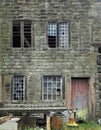 Facade of an old derelict stone house with broken windows and peeling red door with junk outside the front Royalty Free Stock Photo