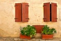 The facade of an old provincial house with two windows, closed by wooden shutters. Garden flowers near the stone house Royalty Free Stock Photo