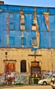 The facade of an old ruinous building is mantled with some blue curtains to protect the pedestrians