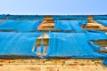 The facade of an old ruinous building is mantled with some blue curtains to protect the pedestrians