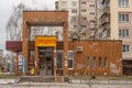 The facade of an old shabby grocery shop in the style of Soviet modernism is littered with chaotically placed advertising banners