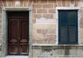 Facade of an old spanish house with dark brown wooden door in a stone frame and black closed shutters with old crumbling tiles Royalty Free Stock Photo