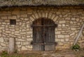 Facade of an old stone brick wall with wooden doors, a small window and thatched roof