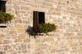 Facade of old stone house with flowers. Traditional exterior of ancient building in sunlight. Windows with flower in village. Royalty Free Stock Photo