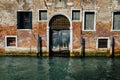 Facade of partially mossy old brick house with wooden vintage door on narrow canal in Venice, Italy. Royalty Free Stock Photo