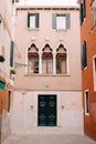 Facade of a three-story peach house in Venice, Italy. Massive green wooden front door, three classic Venetian windows Royalty Free Stock Photo