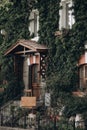 Facade of two-story building is overgrown with ivy, side of entrance with wooden canopy and sign at entrance. Royalty Free Stock Photo