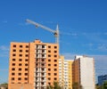 Facade of unfinished brick condominium under construction with crane under blue sky