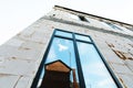 Facade of an unfinished house made of aerated concrete blocks with a large window and a reflection of a wooden shed. Bottom up