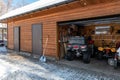 Facade view open door ATV home garage with quad bikes offroad vehicle parked sunny snowy cold winter day. ATV adventure Royalty Free Stock Photo