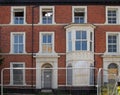 The facades of large abandoned derelict brick houses on a street with boarded up doors and windows behind a fence in southport Royalty Free Stock Photo