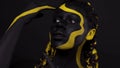 Face art. Dancing woman with black and yellow body paint. Young african girl with colorful bodypaint. An amazing afro