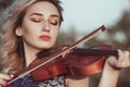 Face of a beautiful girl with a violin under her chin outdoors, young woman playing a musical instrument on nature in solitude,