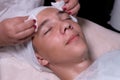 Face of a teenage boy with closed eyes. A beautician wipes a guy`s cheeks and forehead with cotton pads. Dermatological procedure