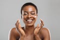 Beautiful afro woman applying cream on her cheeks and sincerely smiling Royalty Free Stock Photo