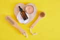 face care set, cosmetic clay, wooden massage brush and amber dropper bottle, yellow background top view