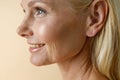 Face closeup of beautiful mature blonde woman smiling away, posing isolated over beige background Royalty Free Stock Photo