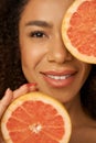 Face closeup of lovely mixed race young woman smiling at camera, posing with grapefruit cut in half Royalty Free Stock Photo