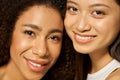 Face closeup of two beautiful happy mixed race young women with perfect glowing skin smiling at camera while posing