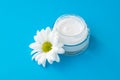 Face cream jar with white chamomile flower on blue background. Herbal lotion in glass bottle, natural cosmetic. Skin care concept Royalty Free Stock Photo