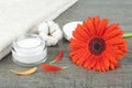 Face cream jar on wooden background with orange gerbera, soft face towel and cotton flower Royalty Free Stock Photo