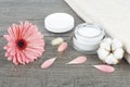 Face cream jar on wooden background with pink gerbera, soft face towel and cotton flower Royalty Free Stock Photo