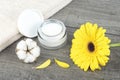 Face cream jar on wooden background with yellow gerbera, soft face towel and cotton flower Royalty Free Stock Photo