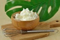 Face cream made of shea butter and argan oil in wooden bowl with whisk on small chopping board