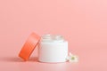 Face cream in white jar with a red cover on a coral background. Cosmetics, beauty. Minimal composition.