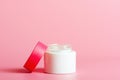 Face cream in white jar with a red cover on a pink background. Cosmetics, beauty. Minimal composition.