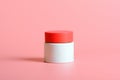 Face cream in white jar with a red cover on a pink background. Cosmetics, beauty. Minimal composition.