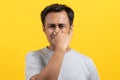 Face expression of human. Asian male smelling disgusted odor and pinching his nose in studio shoot yellow background