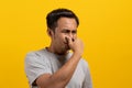 Face expression of human. Asian male smelling disgusted odor and pinching his nose in studio shoot yellow background