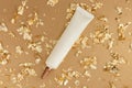 Face and eye cream squeeze cosmetic tube with long nozzle and bronze screw cap, pieces of gold paper on golden background.