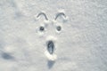 The face of a frightened, shocked smiley painted on the snow, on a sunny winter day. Copy space.